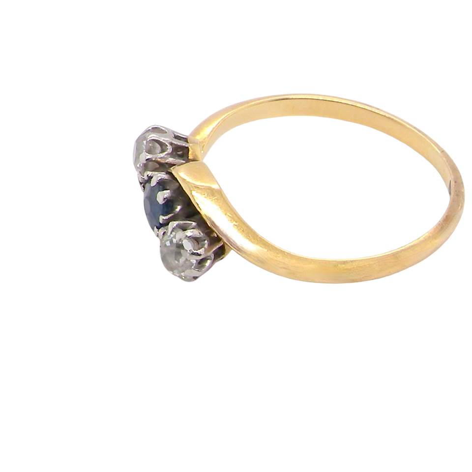 side An 18 carat gold three stone cross over ring.
Centre stone a round sapphire 4mm diameter. Each side a brilliant cut white diamond 4mm diameter (0.25 carats estimated), colour i-k, clarity Si.