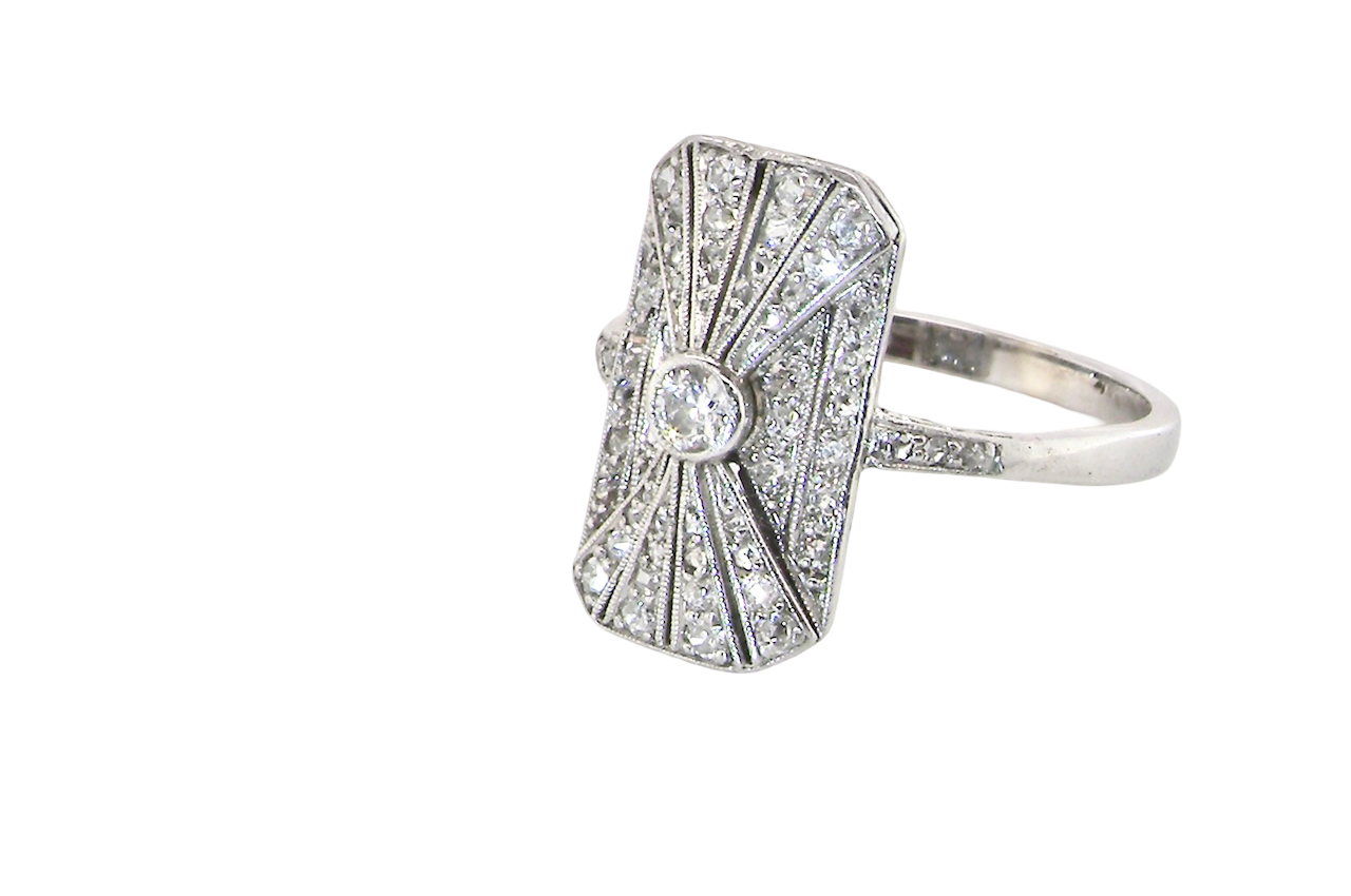 side An Art Deco panel shaped cluster ring. The head measures 16x10mm, depth 3.4mm, and has two fan shaped designs that feature above and below a brilliant cut white diamond centre stone which measures 3.4mm (0.15 carats est)