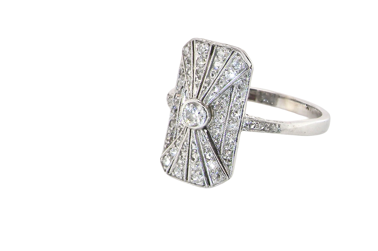 side An Art Deco panel shaped cluster ring. The head measures 16x10mm, depth 3.4mm, and has two fan shaped designs that feature above and below a brilliant cut white diamond centre stone which measures 3.4mm (0.15 carats est)
