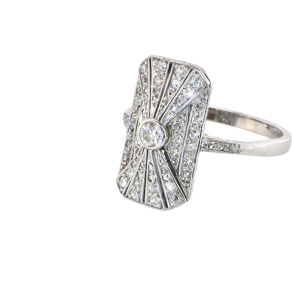 side An Art Deco panel shaped cluster ring. The head measures 16x10mm, depth 3.4mm, and has two fan shaped designs that feature above and below a brilliant cut white diamond centre stone which measures 3.4mm (0.15 carats est)