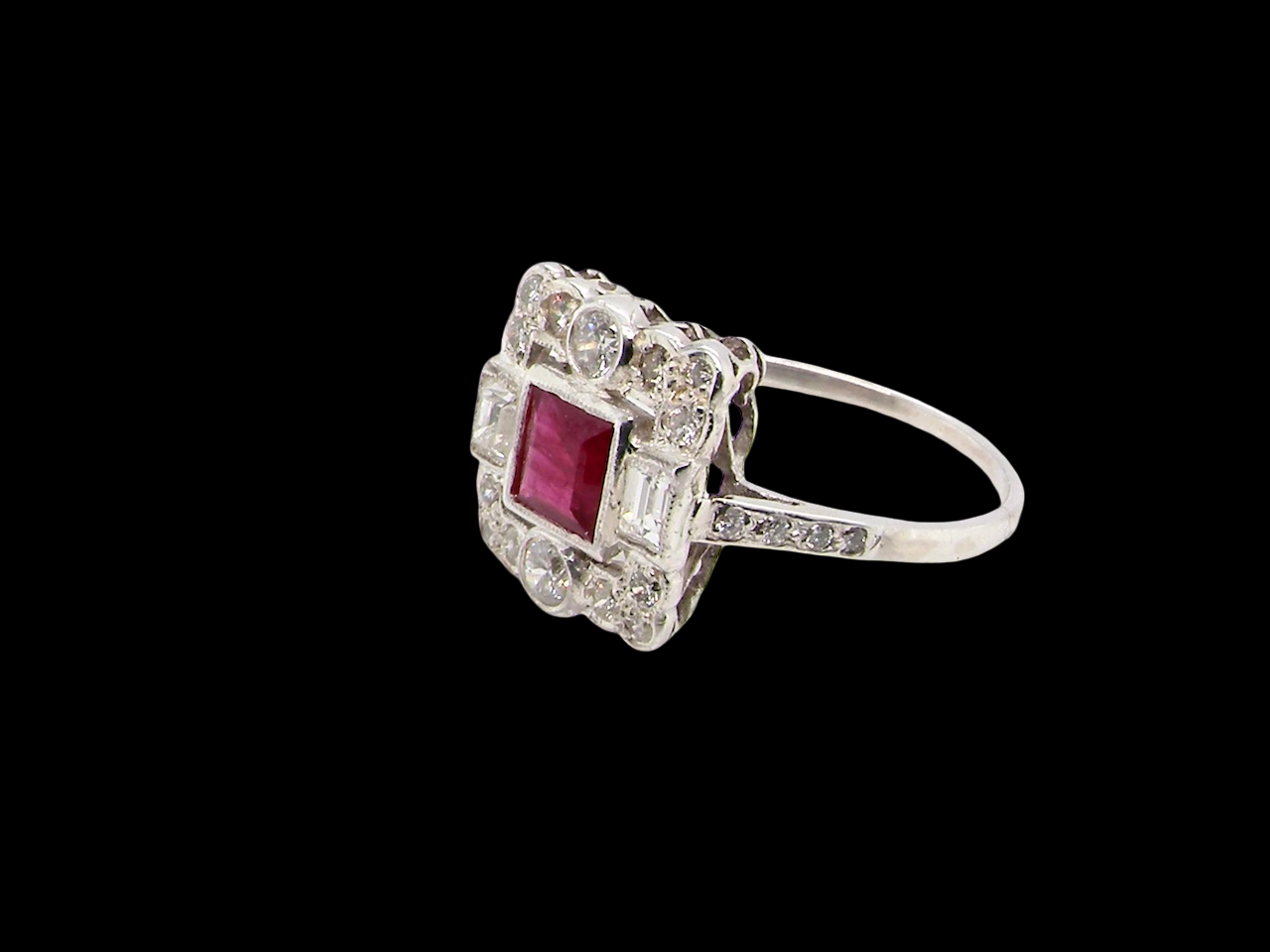 side An Art Deco style cluster ring. Set to the centre a square 5x5mm ruby, rub over setting and complimented by a surround of mixed cut white diamonds.