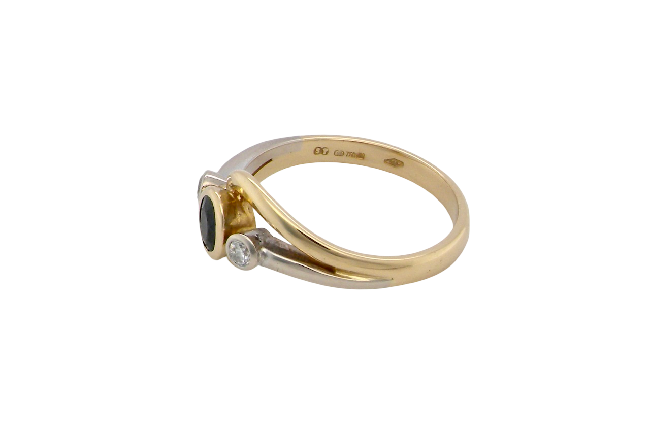 side An elegant 18 carat gold three-stone ring featuring a rich, oval-cut dark blue sapphire at the centre, measuring 5 × 4mm, secured in a classic rim (bezel) setting.