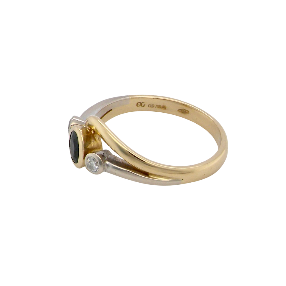side An elegant 18 carat gold three-stone ring featuring a rich, oval-cut dark blue sapphire at the centre, measuring 5 × 4mm, secured in a classic rim (bezel) setting.