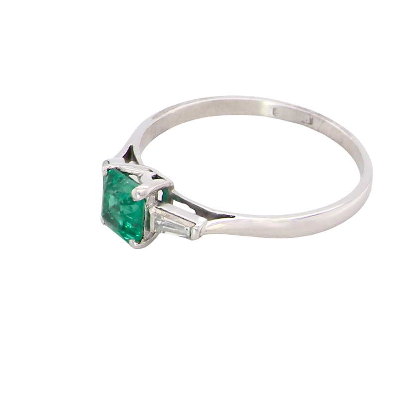 side An elegant and timeless platinum ring featuring a stunning step-cut emerald to the centre, measuring approximately 5.5 x 5.5mm and estimated at 0.80 carats. The emerald displays a vibrant, deep green colour with excellent presence.