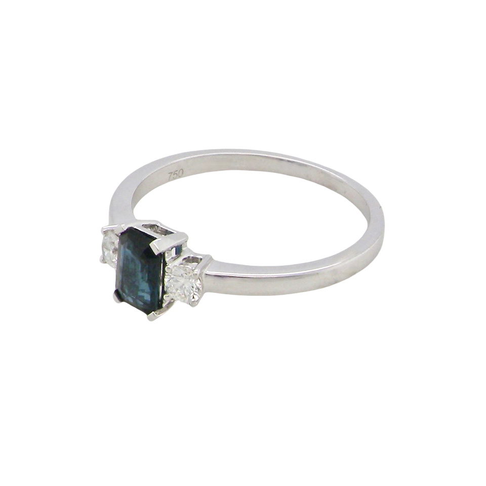 side An elegant three-stone ring crafted in 18 carat white gold, featuring a striking rectangular dark blue sapphire at the centre, measuring 6 × 4 mm and weighing approximately 0.50 carats.