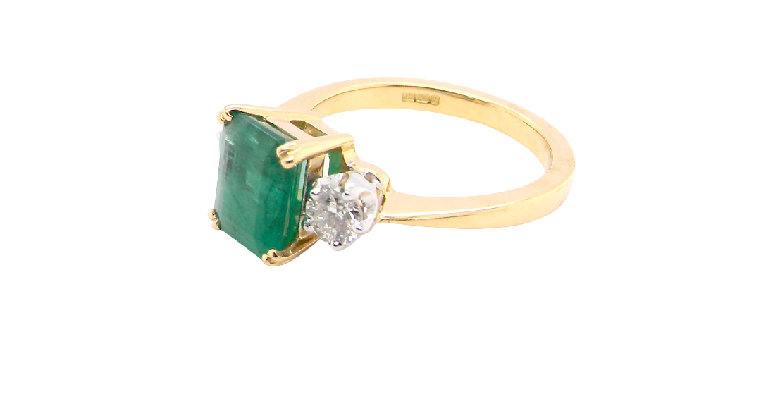 side An exceptional three-stone ring featuring a vibrant step-cut emerald to the centre, measuring 8.6 x 7.0mm and weighing approximately 2.10 carats. The emerald displays a beautiful grass-green colour and is secured in a classic four-claw setting.