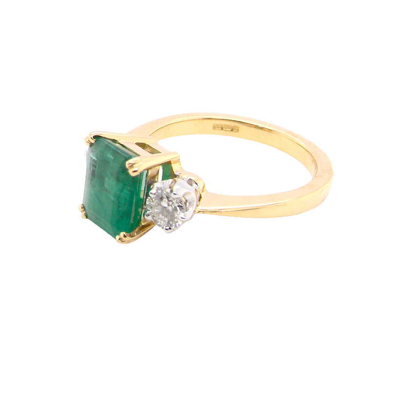 side An exceptional three-stone ring featuring a vibrant step-cut emerald to the centre, measuring 8.6 x 7.0mm and weighing approximately 2.10 carats. The emerald displays a beautiful grass-green colour and is secured in a classic four-claw setting.