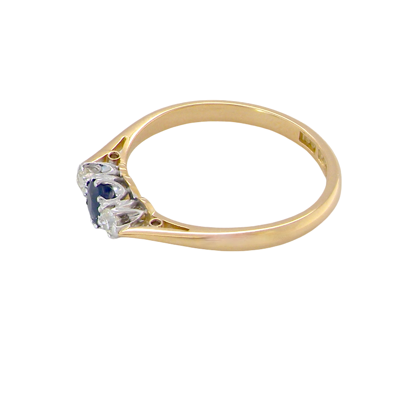side The classic trilogy ring, this features to the centre a round mid to dark blue sapphire and each side a brilliant cut white diamond