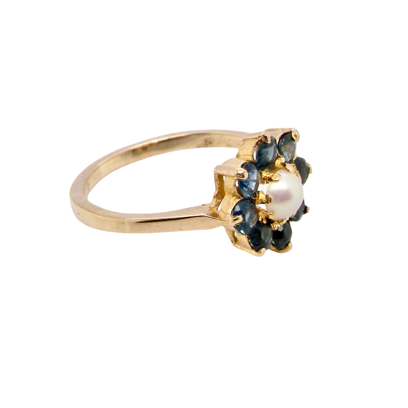 A yellow gold ring featuring a flower-shaped setting with dark blue gemstones and a central white pearl, shown on a plain white background.