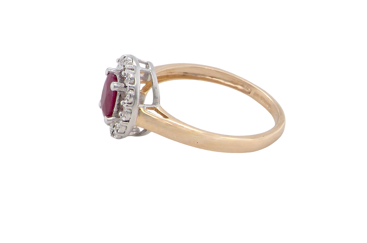side oval ruby measuring 6x4mm (approx. 0.44 carats) in a raspberry red hue. The centre stone is accented by a halo of twelve white diamonds
