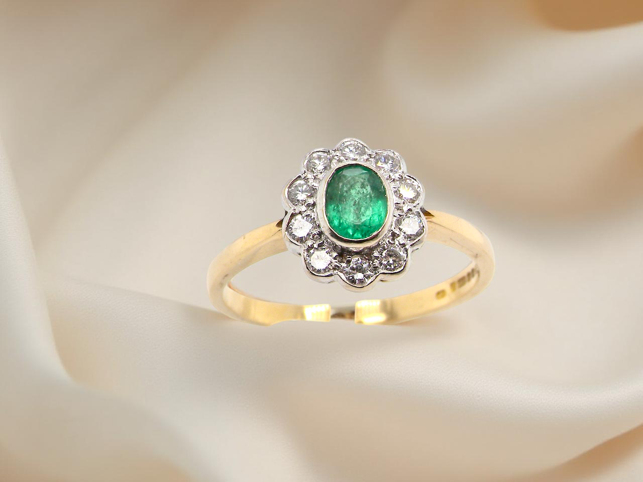 top A beautifully elegant cluster ring featuring a central oval-cut emerald, measuring 5 x 4mm (estimated 0.40 carats).
