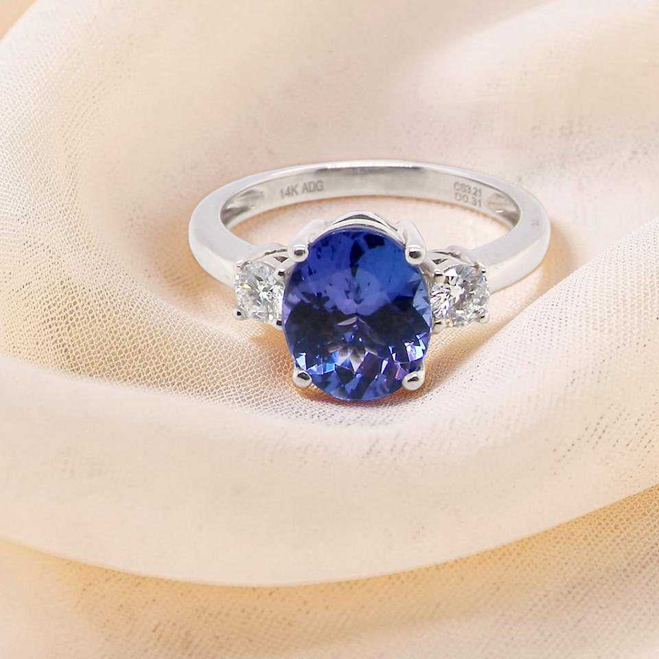 top A three stone ring that features an impressive tanzanite centre stone that measures 10x8mm (3.21 carats confirmed) AAA colour. 