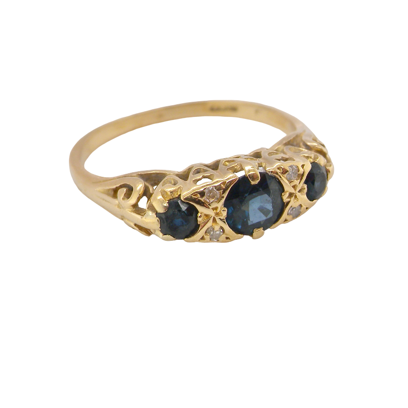 A yellow gold ring featuring three oval dark blue sapphires and small clear accent stones, set against a plain white background.