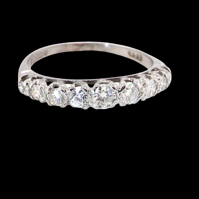 A ring set with a row of round-cut clear gemstones, photographed against a solid black background.