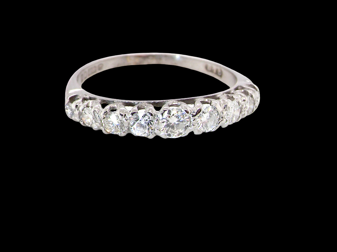 A ring set with a row of round-cut clear gemstones, photographed against a solid black background.