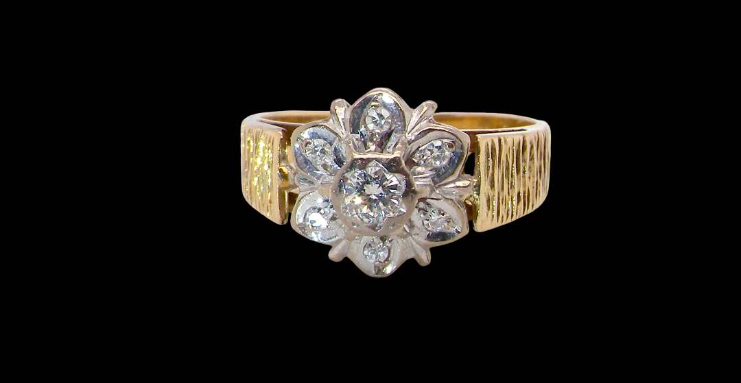 typical design from the 1960s/1970s era, a daisy cluster set with brilliant cut white diamonds and and a bark design finish to both shoulders.