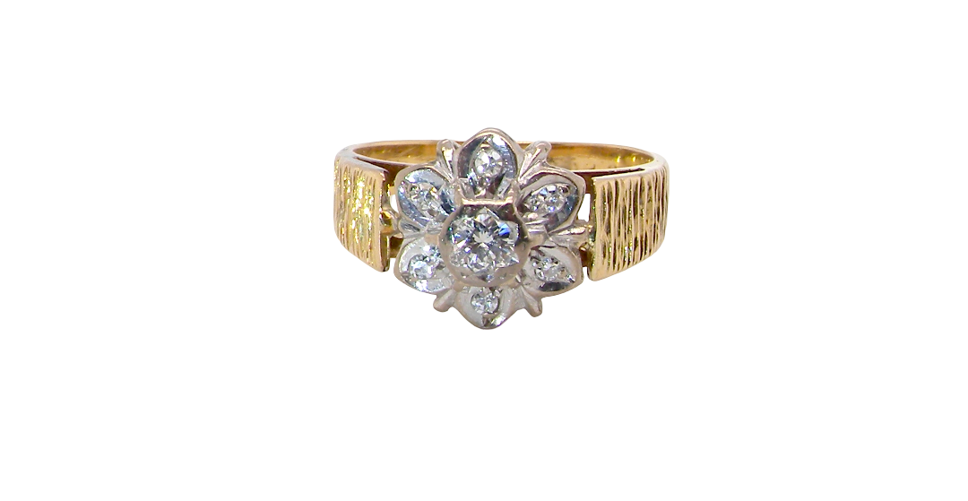 typical design from the 1960s/1970s era, a daisy cluster set with brilliant cut white diamonds and and a bark design finish to both shoulders.
Central diamond measures 2.5mm, and an outer halo of six more diamonds, at 1.2mm each and illusion set in white gold. (Total est carat weight 0.15 carats). Head measures 10mm. The band and shoulders test as 18 carat gold. 