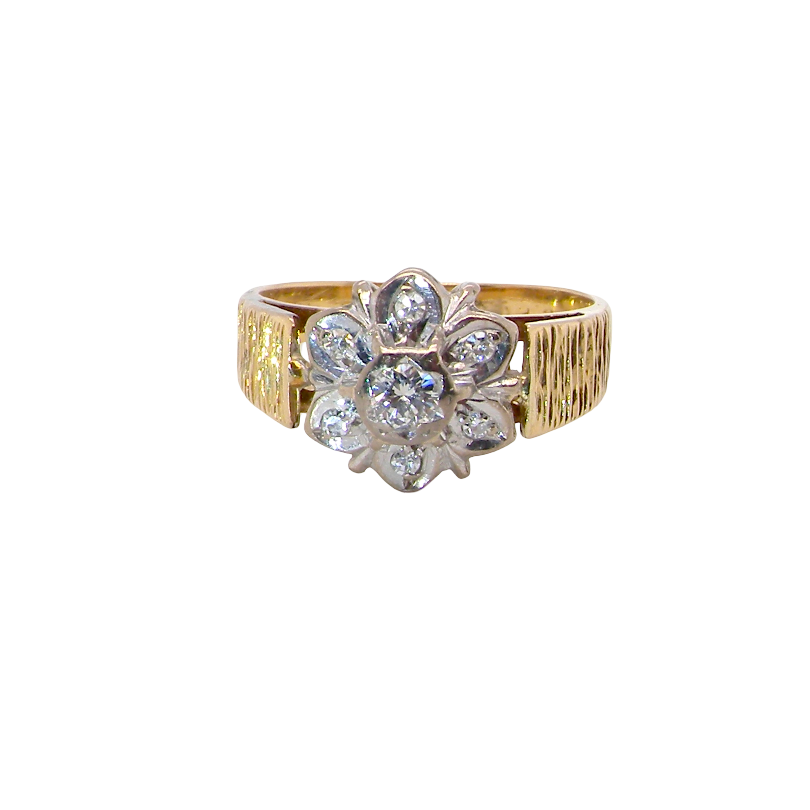 typical design from the 1960s/1970s era, a daisy cluster set with brilliant cut white diamonds and and a bark design finish to both shoulders.
Central diamond measures 2.5mm, and an outer halo of six more diamonds, at 1.2mm each and illusion set in white gold. (Total est carat weight 0.15 carats). Head measures 10mm. The band and shoulders test as 18 carat gold. 