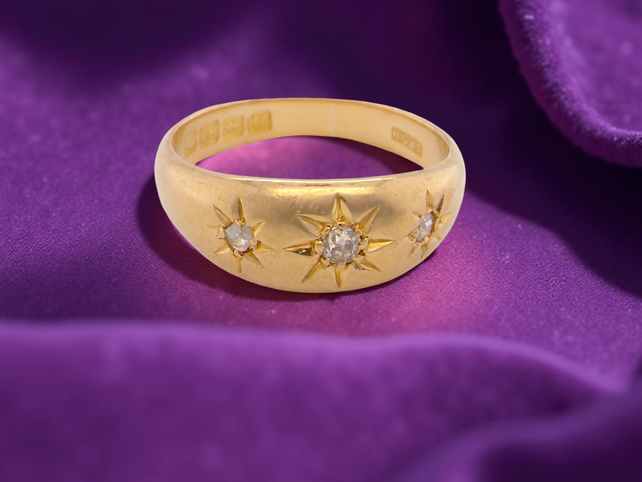 Gold ring with star designs and diamonds on a purple fabric background