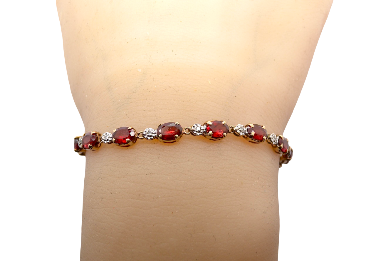 wrist An elegant 9 carat gold bracelet set with sixteen rich red oval-cut garnets, each measuring approximately 6 x 4mm. Between each garnet sits a delicate illusion-set diamond in white gold, creating the appearance of larger stones while adding subtle sparkle. The total diamond weight is estimated at 0.15 carats.