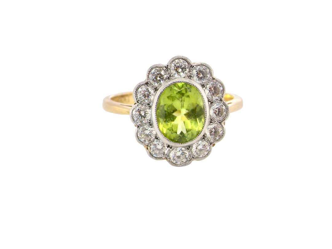 A vintage-style ring featuring an oval green peridot stone surrounded by a halo of small clear stones, set on a yellow gold band.