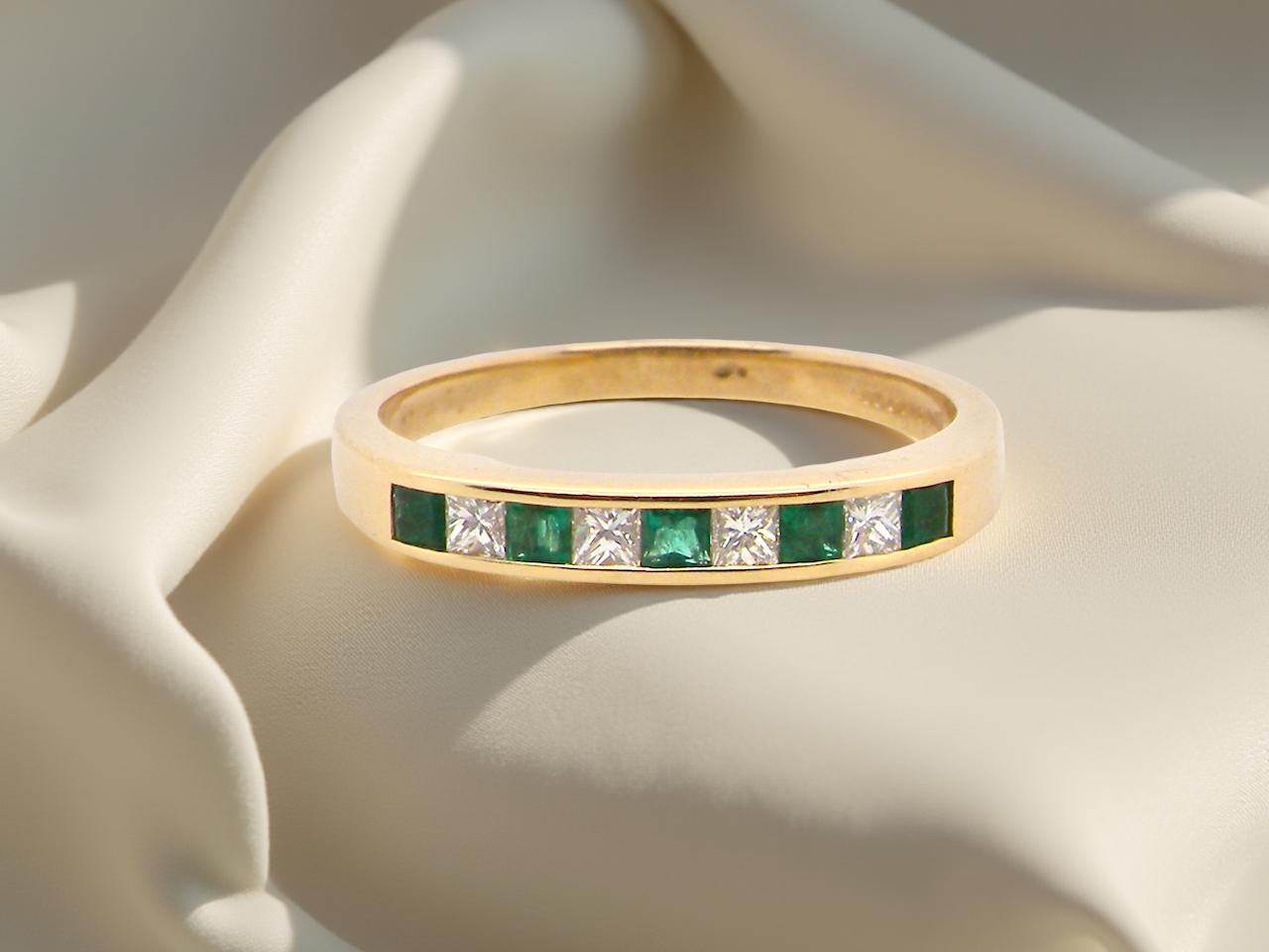 Gold ring with emeralds and diamonds on a soft fabric background