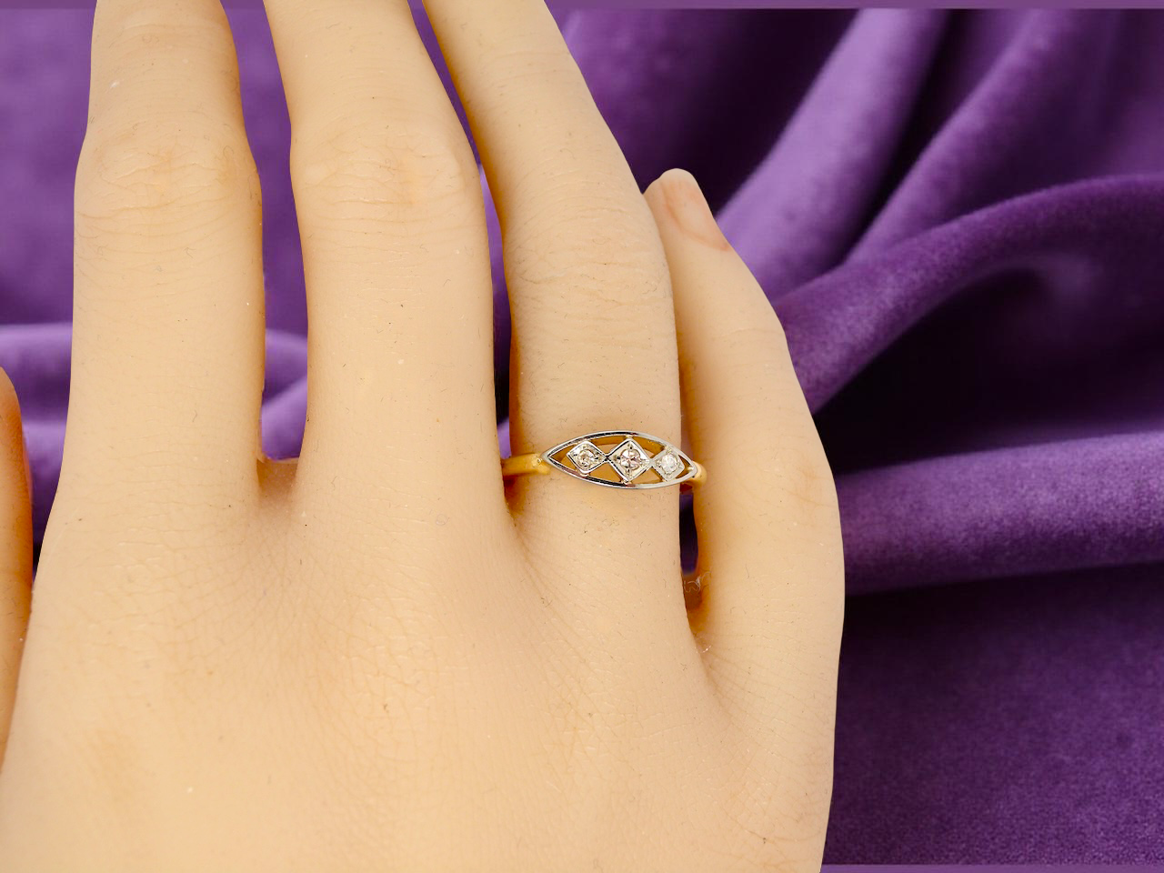 Gold ring with diamonds on a hand against a purple fabric background