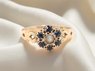 A 15 carat gold dress ring. The centre a small seed pearl, 3mm diameter. Surrounded by 6 sapphires, 