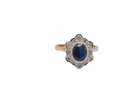 A 9 carat gold cluster ring that features an inky black blue oval cut sapphire. This measures 8x6mm in a safe rim style setting 