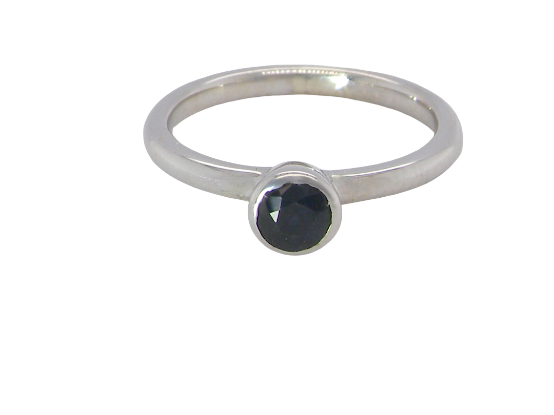 A 9 carat white gold solitaire ring. Features a round dark blue sapphire, 4.6mm diameter (Rim set.
