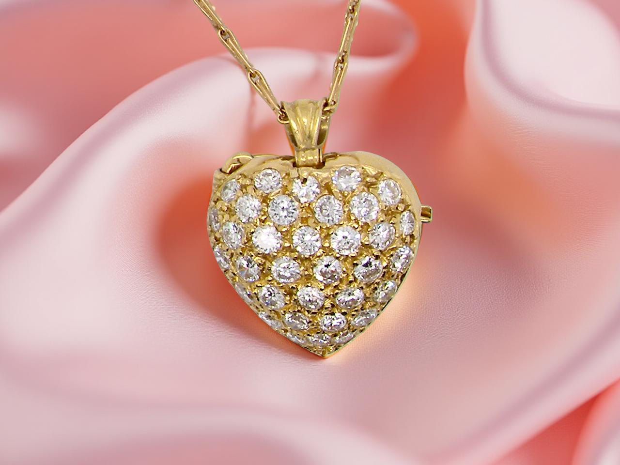 Gold heart-shaped pendant with diamonds on a pink fabric background