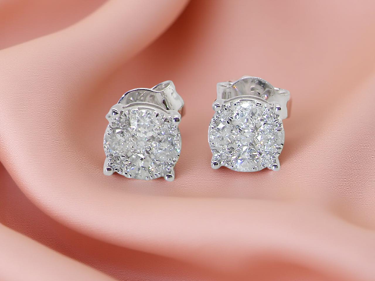 Diamond stud earrings on a person's ear with a soft pink background