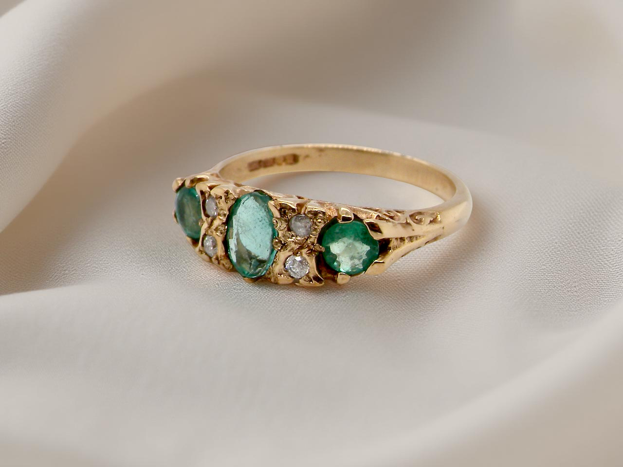 Gold ring with emerald and diamond stones on a beige fabric background