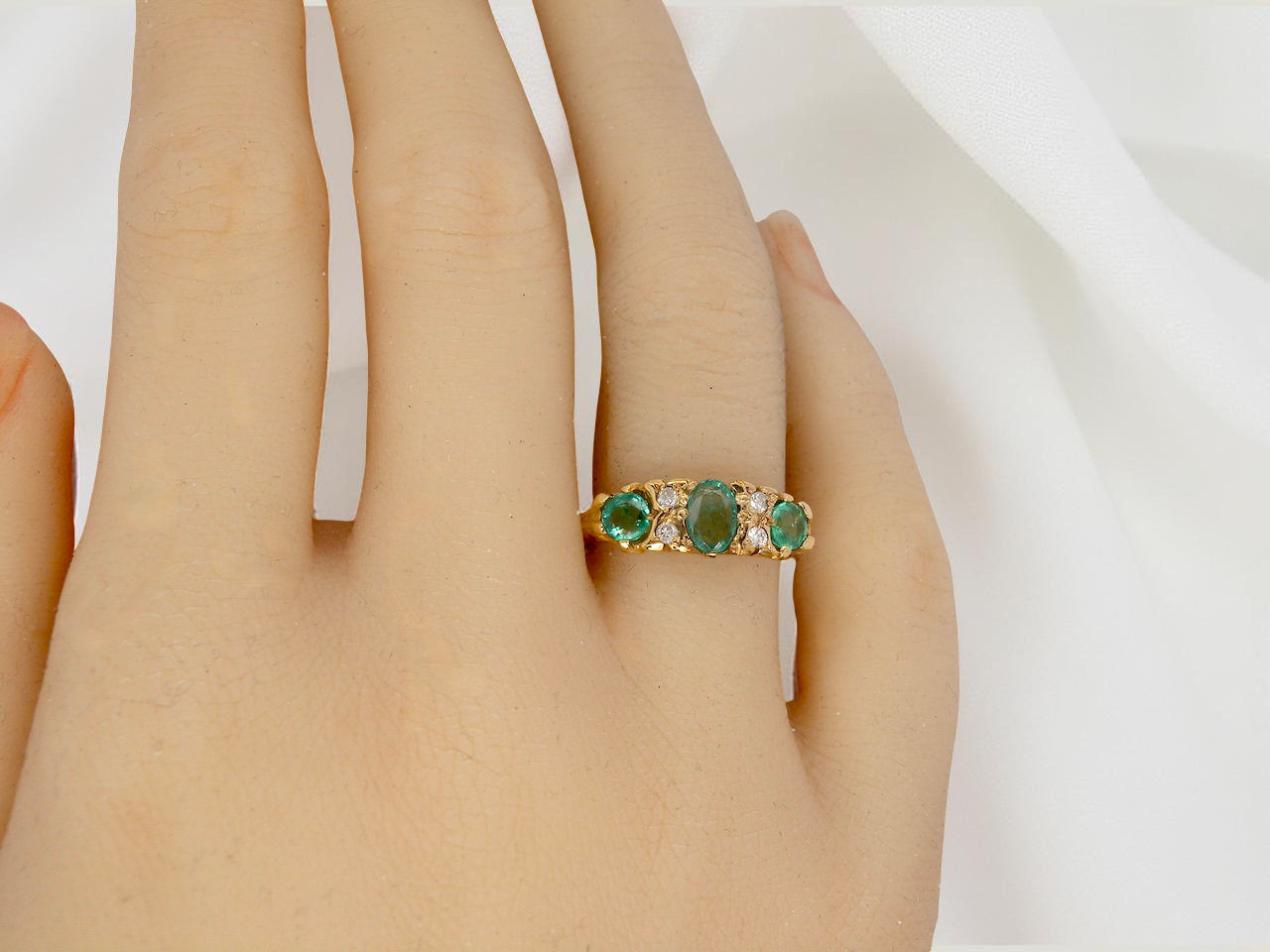 Gold ring with green gemstones on a hand against a white background