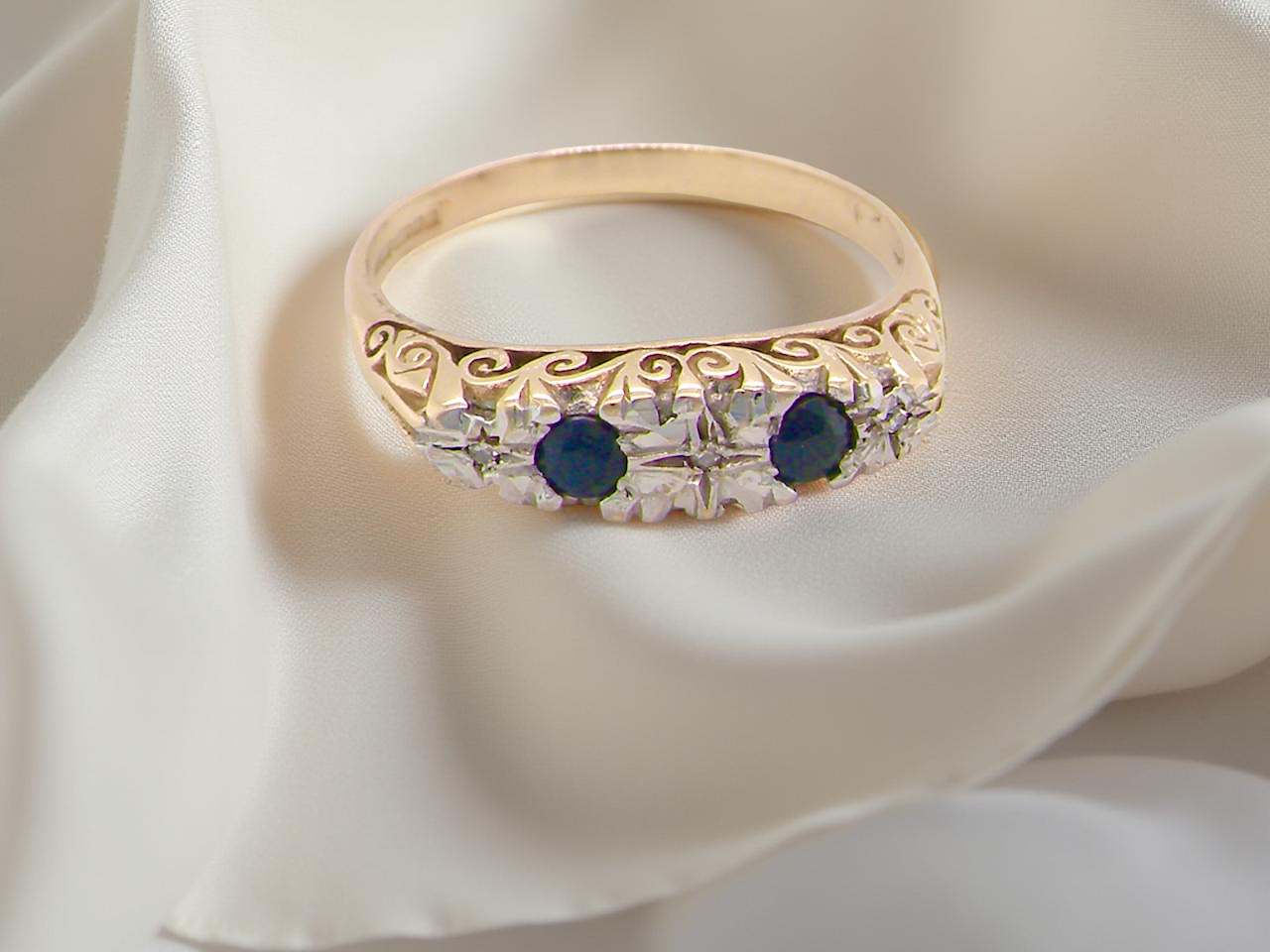 Gold ring with blue and clear gemstones on a white fabric background