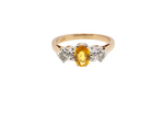 A yellow gold ring featuring an oval-cut yellow center stone flanked by three small round clear stones in a silver-colored setting, shown against a plain white background.