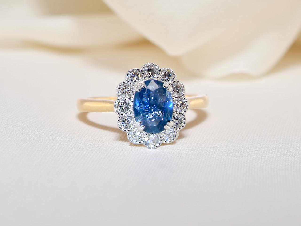 A beautiful cluster ring featuring an oval-cut mid to dark blue sapphire measuring 7 × 5 mm 