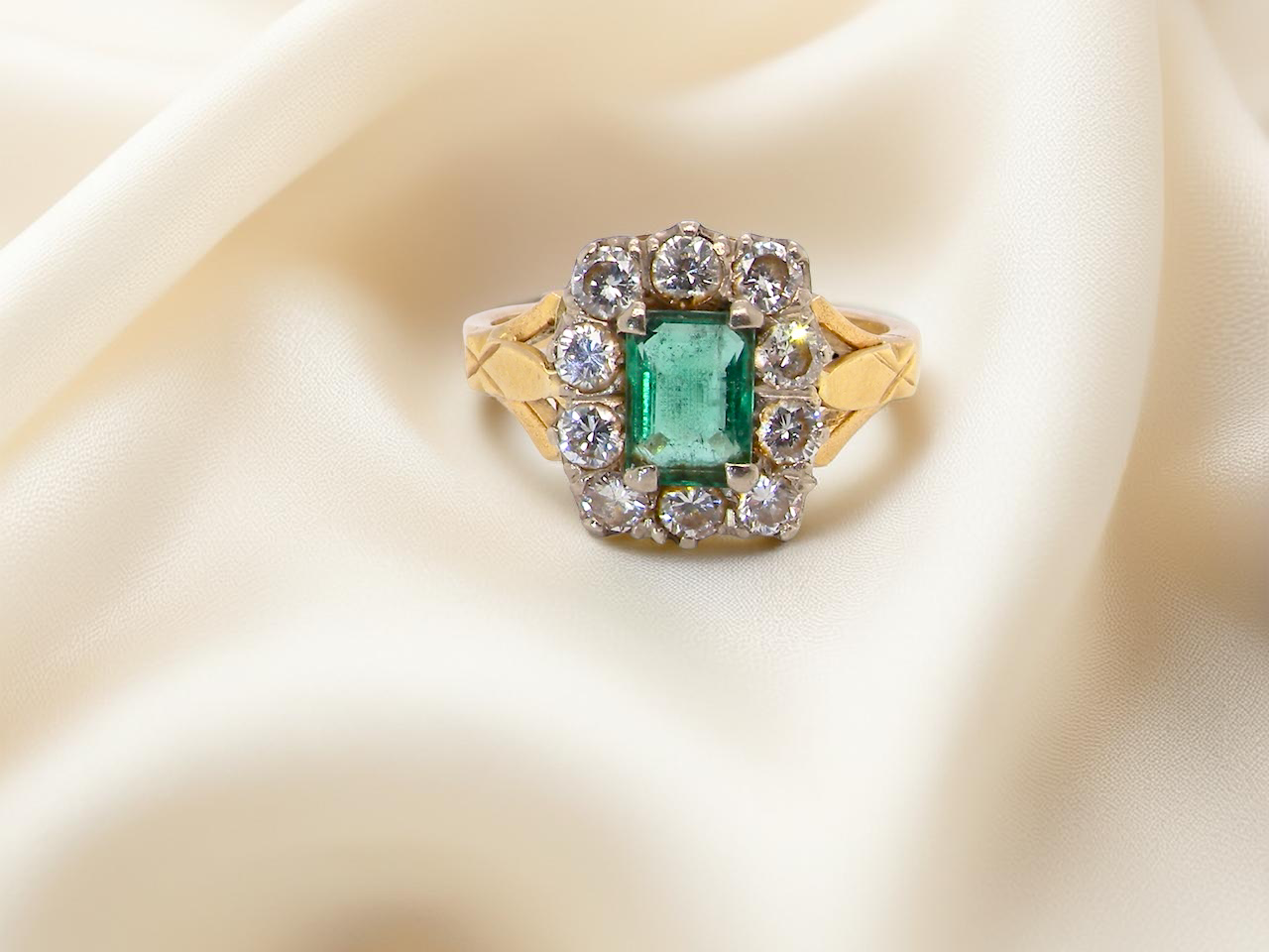 A cluster ring that features a rectangular emerald centre stone, 7x5mm . Deep green colour, 