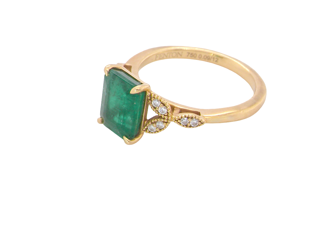 A yellow gold ring featuring a rectangular emerald-cut green gemstone and small clear accent stones on the band, shown on a plain white background.