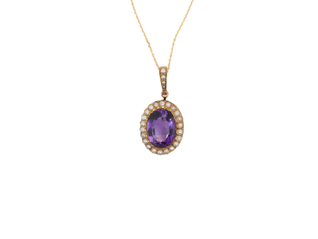 An oval pendant necklace featuring a central purple amethyst gemstone surrounded by a halo of small clear stones, set in yellow gold and suspended from a delicate gold chain against a plain white background.