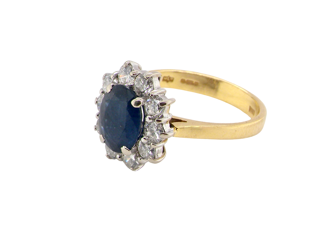 A yellow gold ring featuring a central oval dark blue sapphire surrounded by a halo of clear diamonds, set on a plain white background.