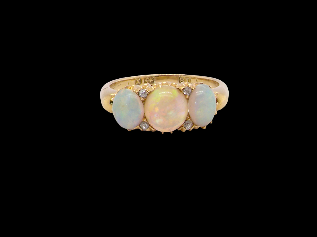 A yellow gold ring featuring three oval opal stones in a row, accented by small clear stones on a solid black background.