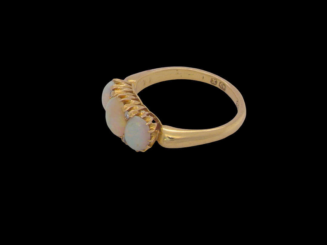 A yellow gold ring featuring three oval cabochon opal gemstones in a textured bezel setting, shown against a solid black background.