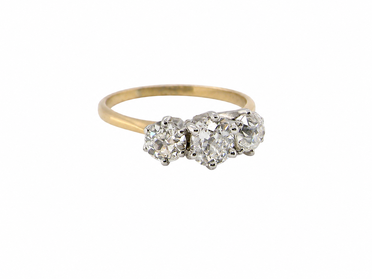 A vintage-style three-stone diamond ring with a yellow gold band and silver-toned settings, shown on a plain white background.