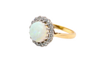 A yellow gold ring featuring a round white opal surrounded by a halo of small clear stones, set against a plain white background.