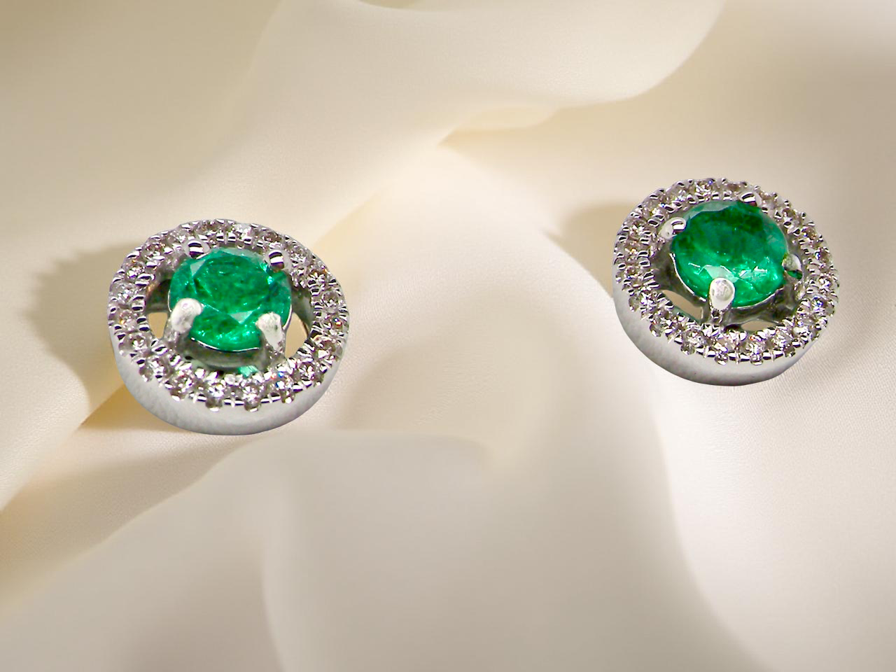 Pair of emerald earrings with diamond accents on a light background