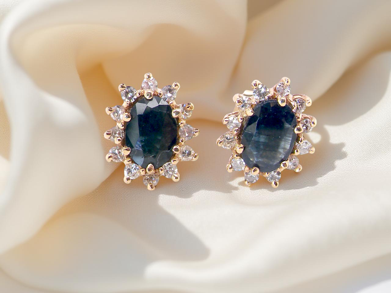 Pair of earrings with blue gemstones and gold accents on a soft fabric background