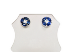 A pair of round stud earrings with deep blue gemstones arranged in a flower shape around a clear central stone, set in silver-toned metal, displayed on a white stand against a white background.