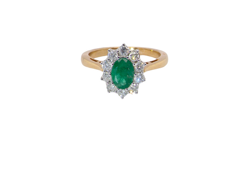A fine traditional emerald and diamond cluster ring, featuring a vibrant oval-cut emerald to the centre measuring approximately 7 × 5 mm 