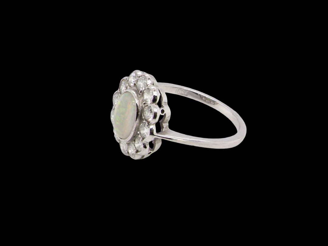 A fine vintage cluster ring. Features to the centre an oval shaped opal, with excellent play of colour, pink to one way, vibrant green to the other with flashes of electric blue also within the body of the gem.
side